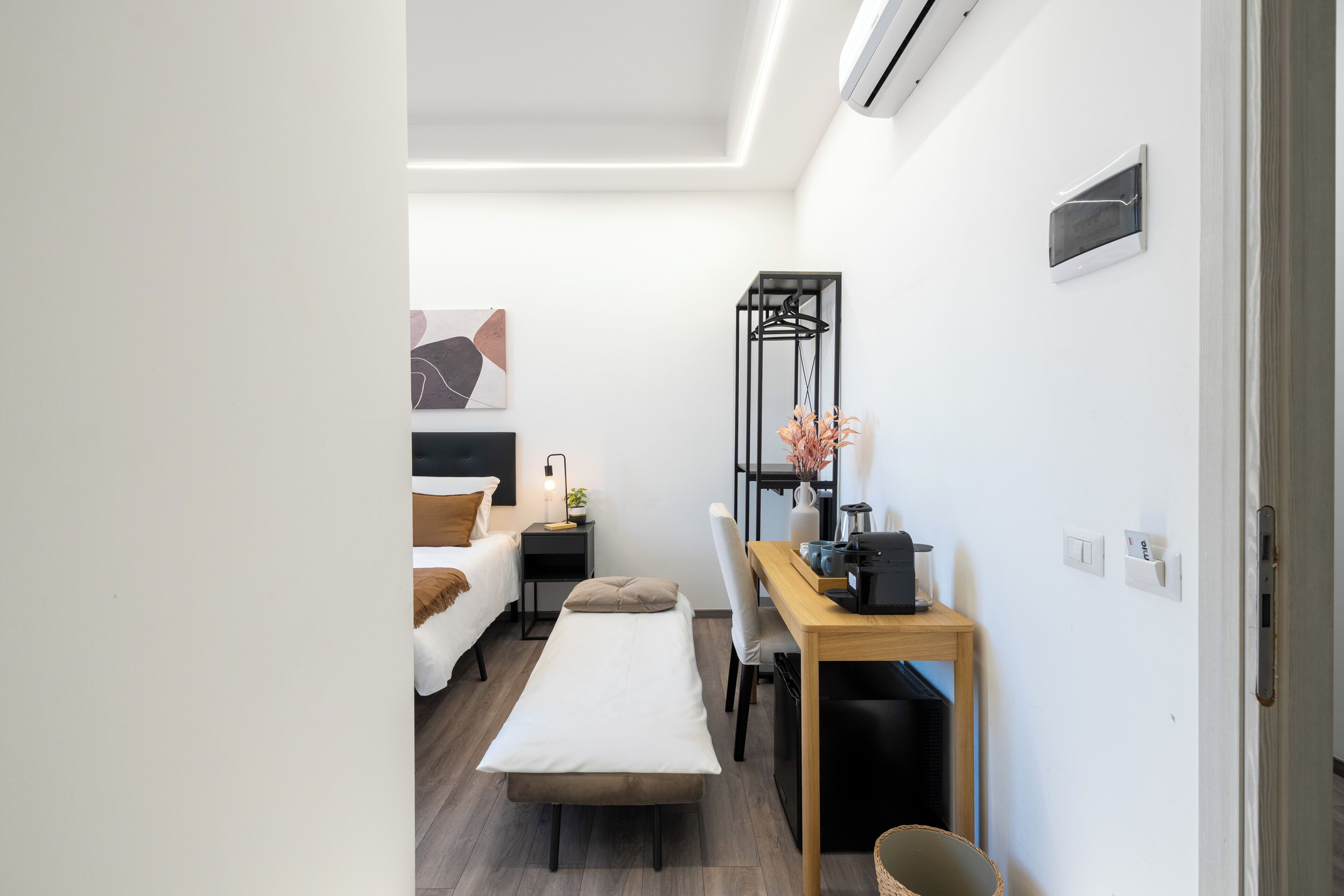 Ein kleines Zimmer mit Bett, Nachttisch, Sessel und Schreibtisch mit Stuhl.