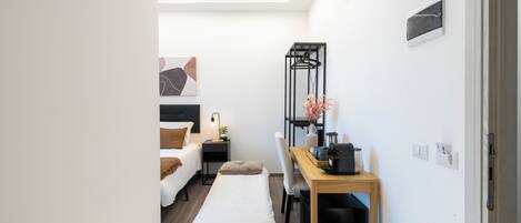 Habitación pequeña con cama, mesita de noche, silla y escritorio con asiento.