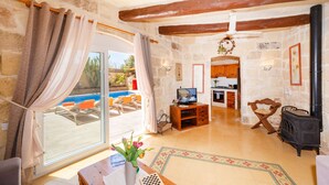 Un salón con suelo de piedra, televisor, muebles de madera, chimenea y vistas a una piscina.