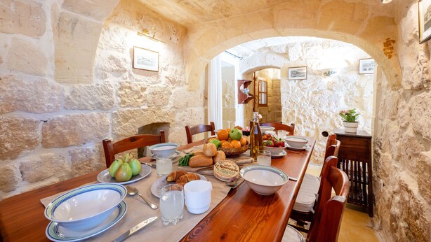 Comedor de paredes de piedra con una mesa de madera dispuesta para el desayuno, incluyendo pan, fruta y huevos.