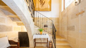 Una escalera con paredes de piedra, un banco de madera, una mesa con un florero y un tapiz colgado.