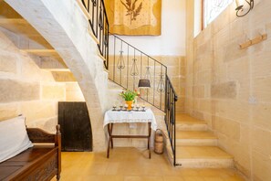 A staircase with stone walls, a wooden bench, a table with a vase of flowers, and a hanging tapestry.