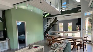 Un interior moderno con comedor, sofá, escalera y vistas al exterior.