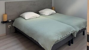 Un dormitorio con tragaluz, una cama con dos almohadas, una lámpara de noche y una mesita.