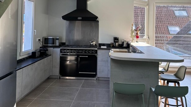 Una cocina moderna con una isla central, horno empotrado y una campana extractora grande.