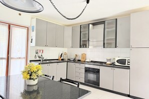 Een moderne keuken met grijze kastjes, een zwart aanrecht en een eethoek met een tafel en stoelen.