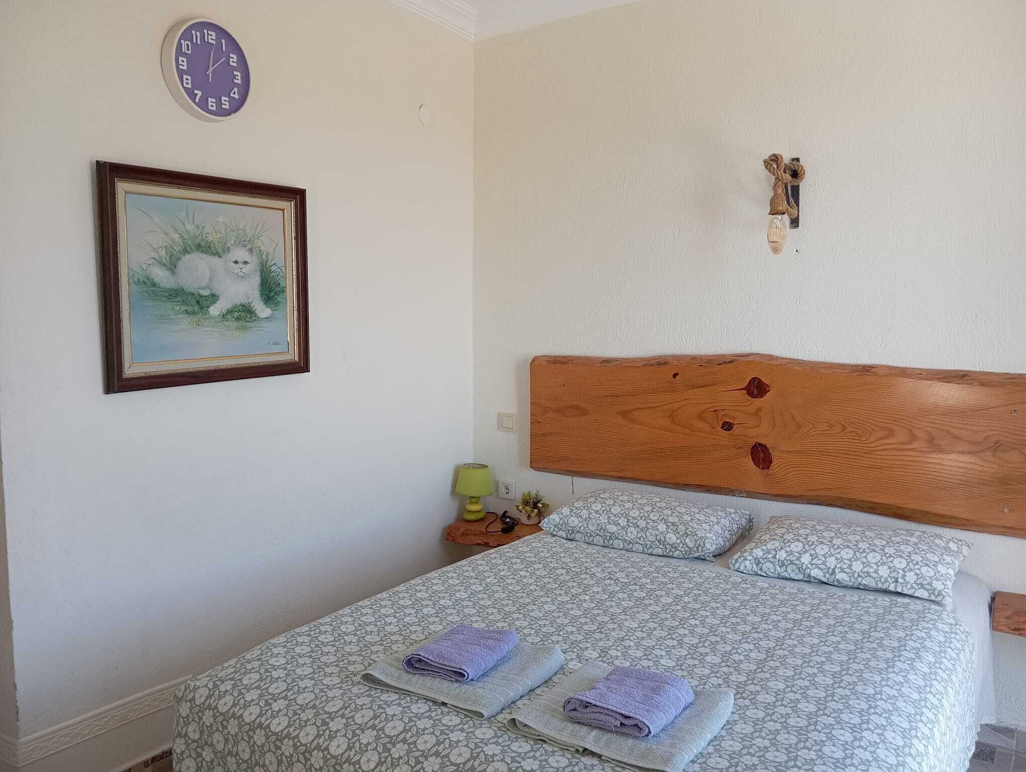 Un dormitorio con cama, un reloj, un cuadro enmarco y un cabecero de madera.