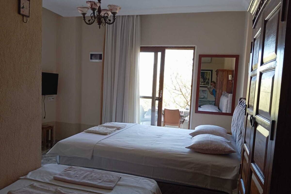A hotel room with two beds, a chandelier, a television, and a window with a view of the outside.