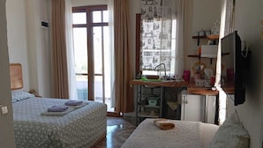 A room with two beds, a kitchenette, a television, and a window with curtains. - W Antic Pansiyon (Datca)