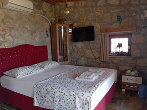 A bedroom with a stone wall, a red headboard, a flat-screen TV, a window with a view, and a bedside table with a lamp.