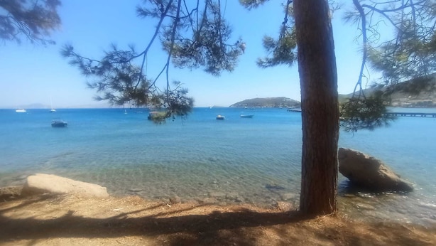 A beach with clear water, boats, and a distant island. - W Antic Pansiyon (Datca)