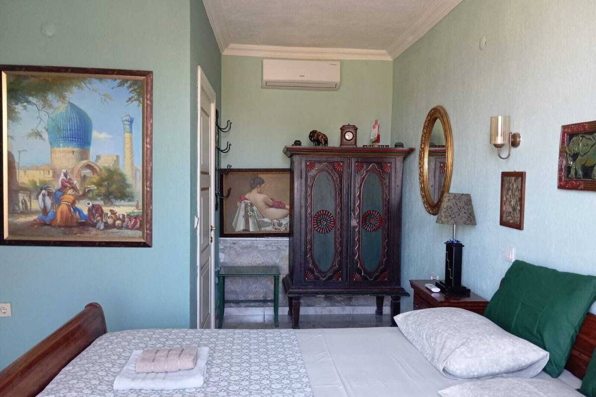 A bedroom with a bed, a dresser, a mirror, and a painting.