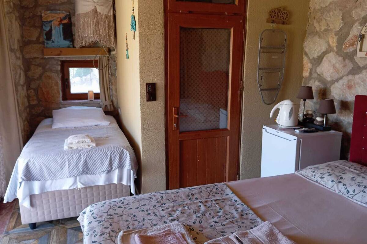 A room with two beds, a small kitchenette, a stone wall, and a wooden door.