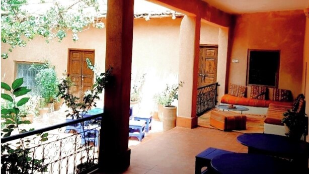 A covered outdoor area with a seating arrangement, a balcony with a railing, and potted plants. - Tighremt Assif Melloul (Anergui)