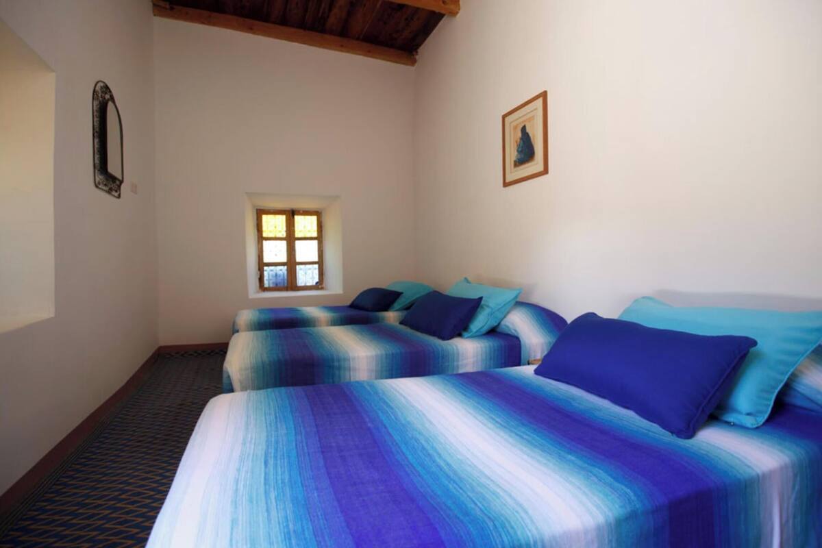 Ein Zimmer mit zwei Betten, einem Fenster, einem Spiegel und einem gerahmten Bild an der Wand.