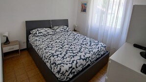 Ein Schlafzimmer mit einem Bett, einem Nachttisch, einem Schreibtisch und einem Fenster mit Vorhängen.