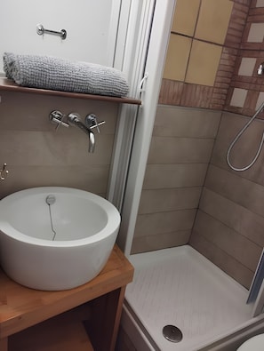 Un bagno con un lavandino bianco, un asciugamano su uno scaffale e una doccia.