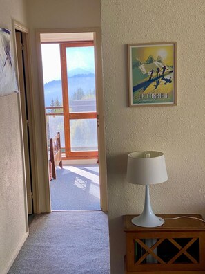 Ein Zimmer mit einer Tür, die auf einen Balkon führt, einem gerahmten Poster an der Wand und einer Lampe auf einem Holznachttisch.