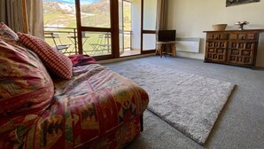 Un soggiorno con divano, televisione, mobiletti in legno e vista su un paesaggio montuoso attraverso ampie finestre.
