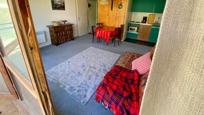 Una stanza con un tavolo da pranzo, sedie, una tovaglia rossa, un angolo cottura con un pensile verde e una coperta decorata sul pavimento.