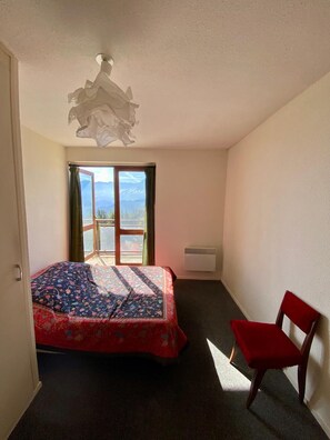 Ein Schlafzimmer mit Bett, Sessel, Fenster mit Blick und Deckenleuchte.