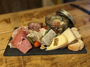 Una tabla de fiambres con diversos embutidos, quesos y pepinillos sobre una tabla de pizarra.