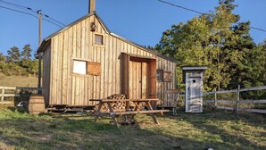 A wooden cabin with a porch, a small shed, and a dog on the grass. - Tiny House “La Petite Maison Dans La Prairie” – Nature Retreat Inspired by Your Favorite Series (Lafarre)