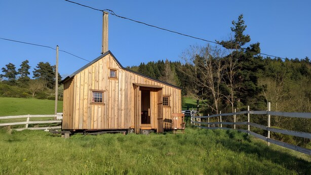 A wooden cabin with a chimney, a door, and a window. - Tiny House “La Petite Maison Dans La Prairie” – Nature Retreat Inspired by Your Favorite Series (Lafarre)