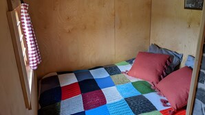 A small, cozy room with a wooden wall, a single bed with a colorful quilt, and a small wall-mounted light fixture. - Tiny House “La Petite Maison Dans La Prairie” – Nature Retreat Inspired by Your Favorite Series (Lafarre)