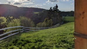 A grassy field with a white fence and a wooden structure. - Tiny House “La Petite Maison Dans La Prairie” – Nature Retreat Inspired by Your Favorite Series (Lafarre)