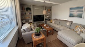Ett vardagsrum med en grå soffa, ett soffbord i trä, en tv och en bokhylla.