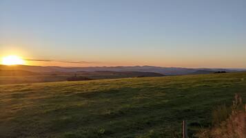 A grassy field with a fence in the foreground and a sunset in the background.