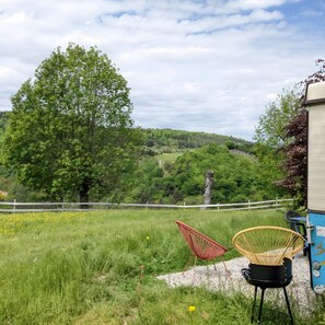 A grassy outdoor area with a large tree, a white fence, and two chairs. - The Vintage Caravan at the Source of the Loire (Lafarre)