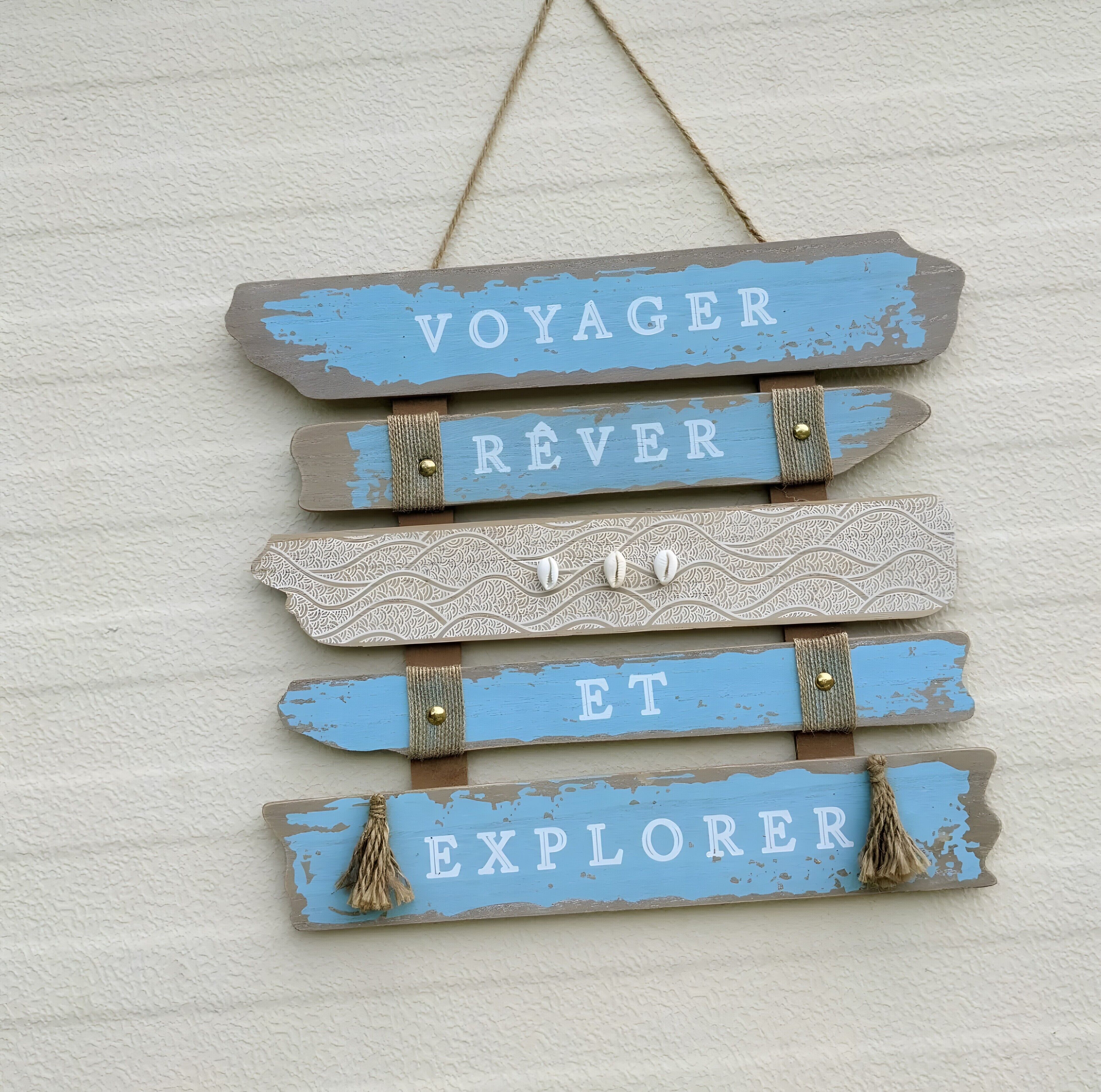 Een wandbord met de woorden 'VOYAGER', 'RÊVER', 'ET' en 'EXPLORER' in een rustieke stijl.