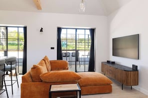 A modern living room with a sectional sofa, a TV, and a dining area with chairs and a table.