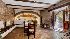 Een interieur met zichtbare bakstenen muren, een stenen openhaard en een eetgedeelte met houten stoelen en een tafel.