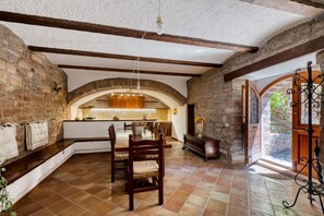 Un interior amb parets de maó a la vista, una llar de pedra i una zona de menjador amb caires de fusta i una taula.