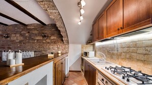 Une cuisine avec un mur en pierre, des placards en bois, une cuisinière à gaz et un four à micro-ondes.