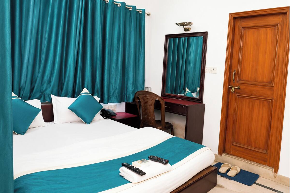 Ein Hotelzimmer mit einem Bett, einem Schreibtisch, einem Spiegel, einer Tür und einem Paar Hausschuhen auf dem Boden.