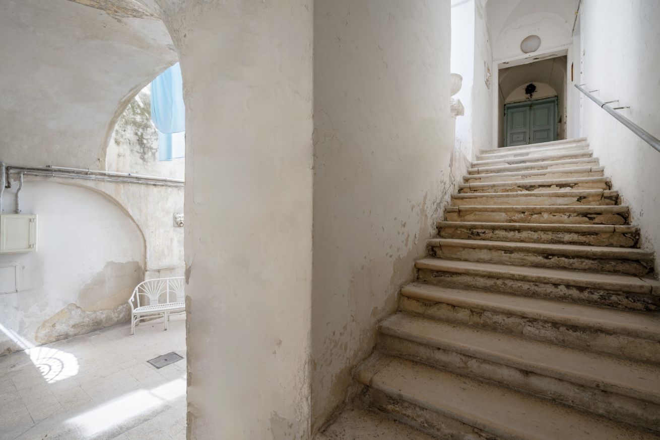 Eine Treppe führt zu einer Tür mit blauem Rahmen, einer weißen Bank und einem Metallgeländer.
