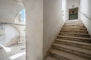 Eine Treppe führt zu einer Tür mit blauem Rahmen, einer weißen Bank und einem Metallgeländer.