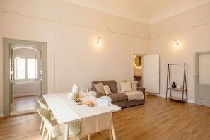 Ein geräumiges Zimmer mit Esstisch, einer Couch und einem kleinen Regal.