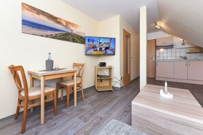 A room with a dining table, chairs, a TV, a small shelf, and a kitchen area. - Quietly located yet central apartment directly on the North Sea coast. (Esens)
