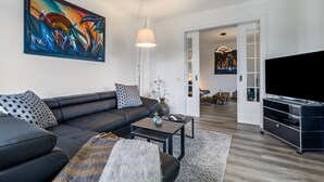 En moderne stue med en sort lædersofa, et billede, en lampe og et fjernsyn.