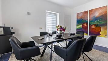 Un coin repas avec une table dressée pour quatre personnes, des chaises noires, un vase avec des fleurs et deux tableaux abstraits accrochés au mur.
