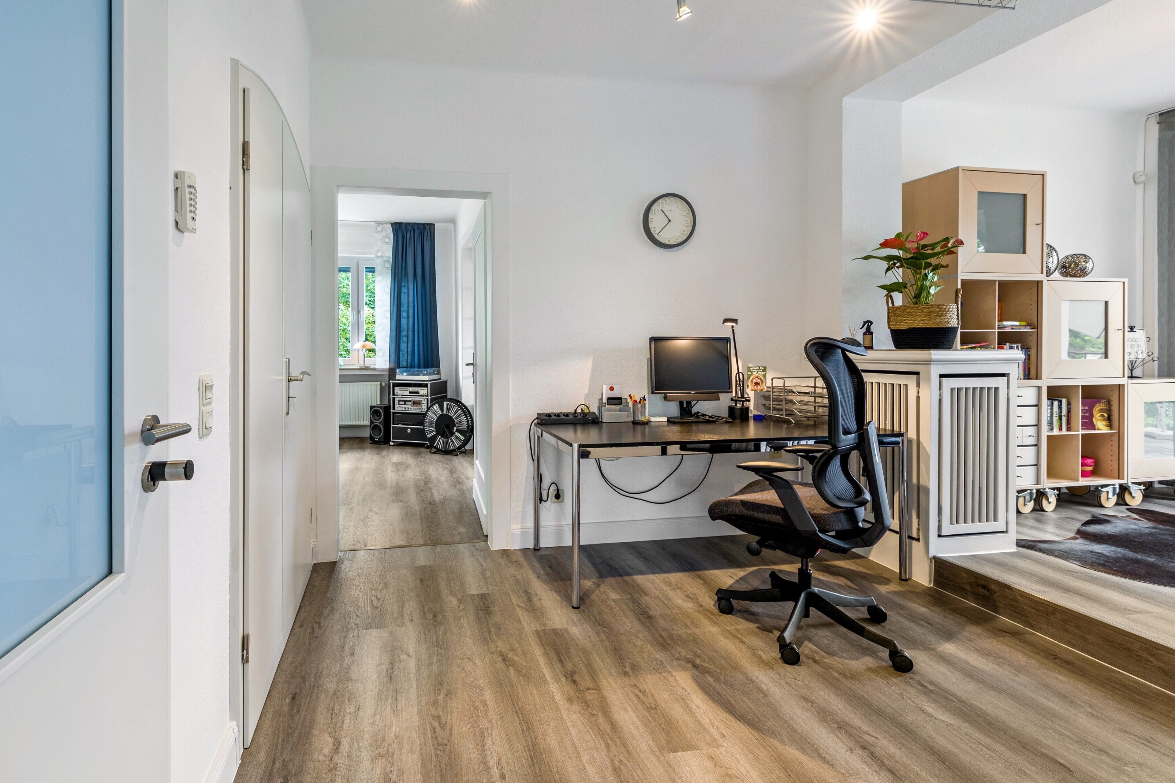 Ein moderner Arbeitsplatz mit Schreibtisch, Stuhl, Computer und einer Wanduhr.