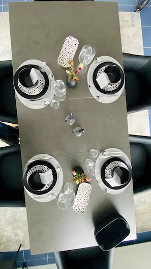 A dining table set for four with black and white patterned plates, clear glasses, and a vase with flowers. - Relax or Work – Modern Apartment in Gevelsberg with Balcony and Air Conditioning (Gevelsberg)