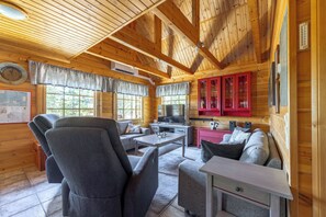LâintĂ©rieur dâun chalet en bois comprend un canapĂ©, des fauteuils, une table Ă manger et un coin cuisine.