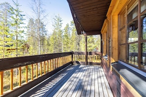 Une terrasse en bois avec une rambarde, de grandes fenĂȘtres et une vue sur une forĂȘt.