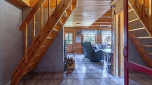 A wooden interior with a staircase, a living area with a sofa and table, and a fireplace.